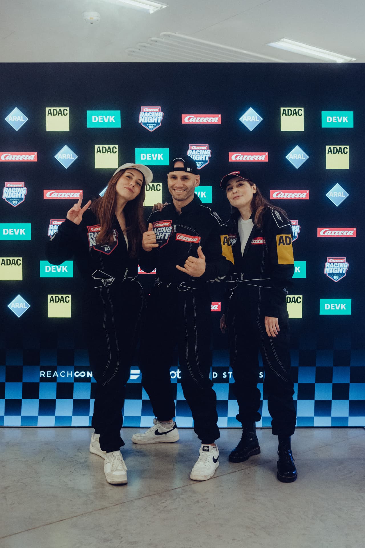 Verena im Racing-Anzug mit Flying Uwe und Veyla vor der Sponsor-Wand der Carrera Racing Night