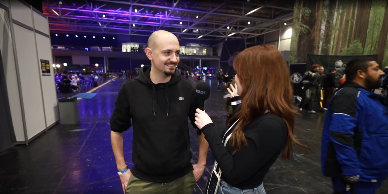 Verena interviewt mit dem Mikrofon einen Aussteller mitten in der Halle der Gamevasion