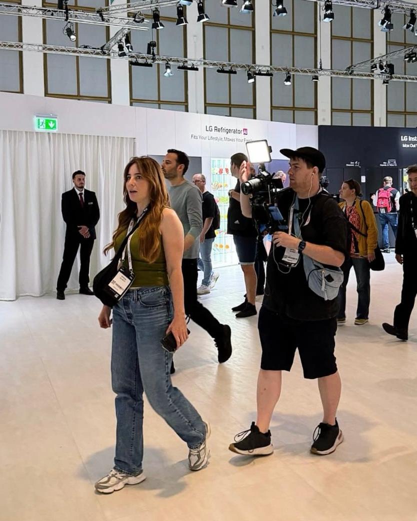 Verena läuft mit ihrem Kamerateam über die IFA-Messehalle, im Hintergrund die Messestände